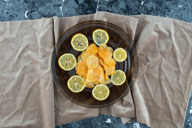 Potato chips in a glass plate on pieces of fabric on marble.