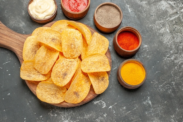 Бесплатное фото Картофельные чипсы, специи и майонез с кетчупом на деревянной разделочной доске на сером столе