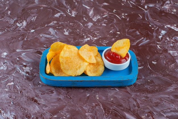 Potato chips with ketchup in a wooden plate on the marble surface