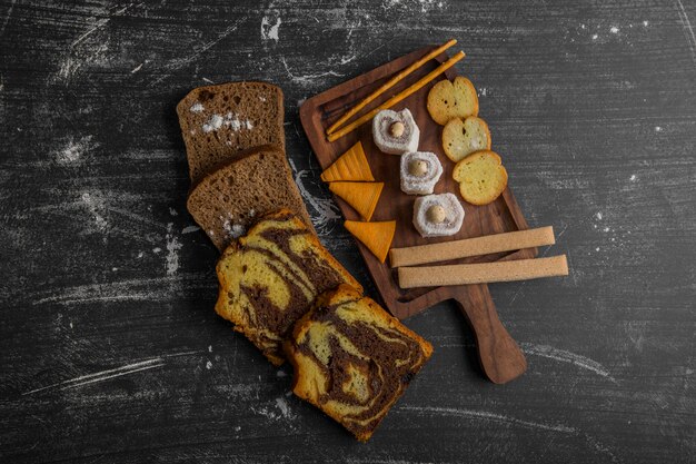 Potato chips with pastry products on a wooden platter and bread slices aside in the middle