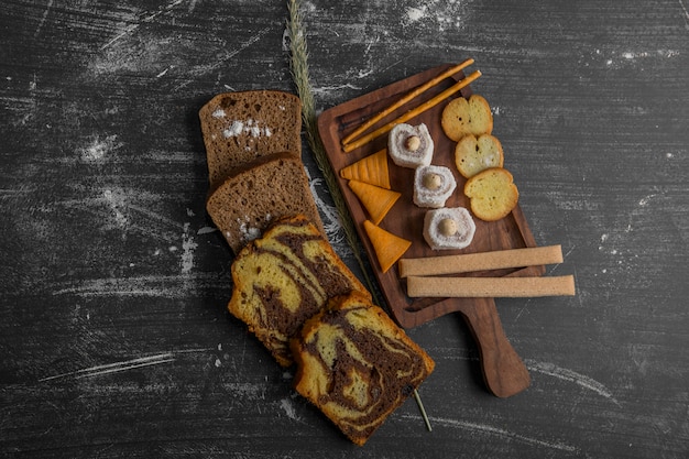 Potato chips with pastry products on a wooden platter and bread slices aside