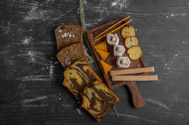 Potato chips with pastry products on a wooden platter and bread slices aside