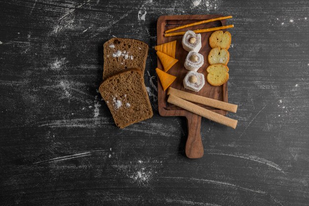 Potato chips with pastry products on a wooden platter served with dark bread