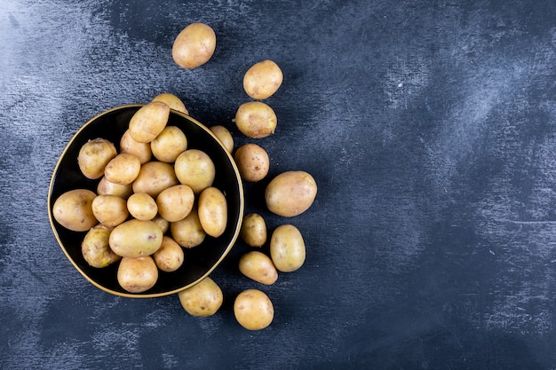 Potatoes in a bowl and around, on a dark table