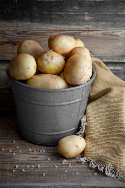 Potatoes in a gray bucket on a dark wooden background. side view.