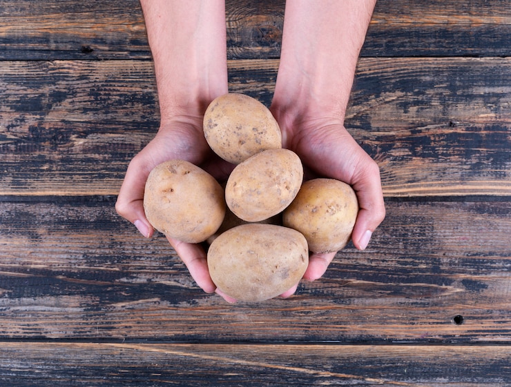Free Photo potatoes in a man's hands on a dark wooden table