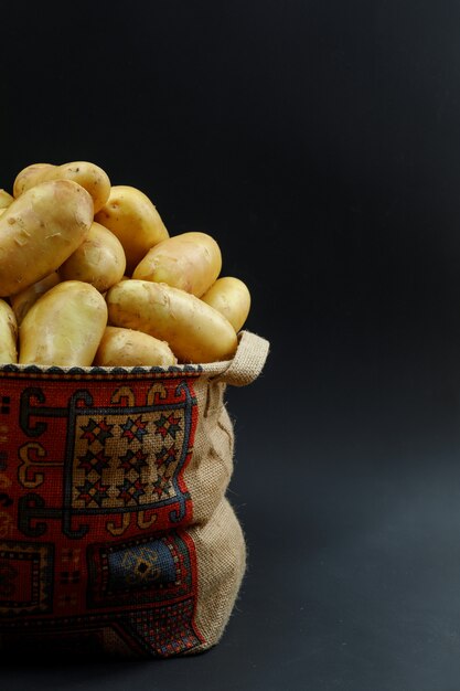 Potatoes in a patterned sack on a dark table. side view.