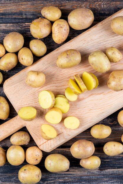 Potatoes and sliced potatoes on a cutting board on a wooden table