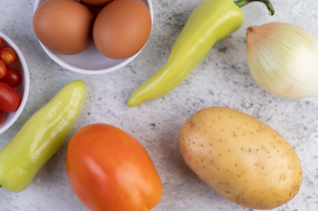 Potatoes, tomatoes, bell peppers, onions and eggs on cement