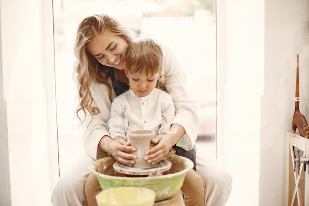 Pottery classes. Young caucasian mother teaching her son. Son making clay pot on potter wheel.