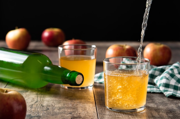 Pouring apple cider drink into a glass on wooden table