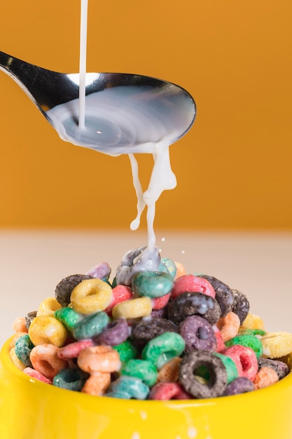 Pouring milk with spoon on bowl with cereals