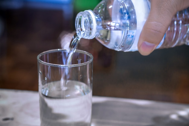 Pouring purified fresh drink water from bottle on glass table background