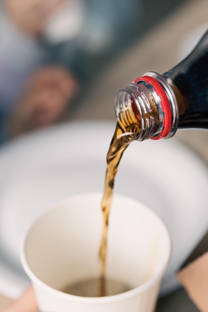 Pouring soda drink from bottle to glass close up