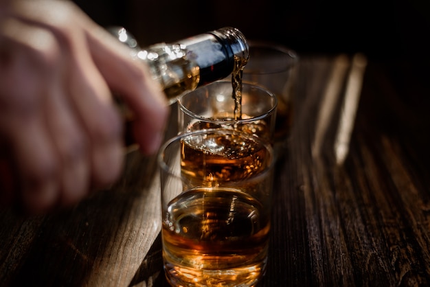 Pouring strong alcohol drink into the glasses which are on the wooden table