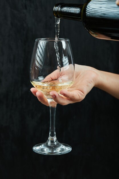 暗い表面のワイングラスに白ワインを注ぐ