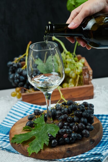 Pouring wine into the glass with plate of grapes on white table