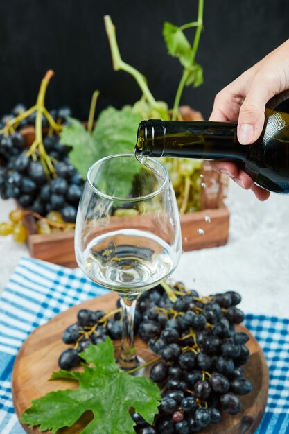 Pouring wine into the glass with plate of grapes on white table