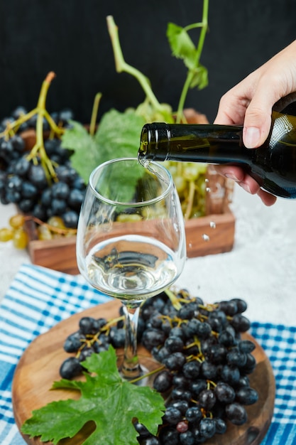 Pouring wine into the glass with plate of grapes on white table