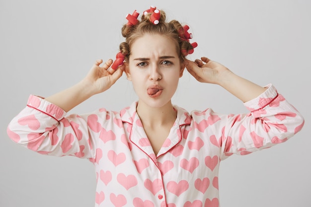 Pouting cute teenage girl take-off hair curlers, wearing nightwear