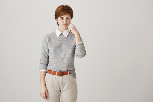 Pouting redhead girl with short haircut posing against the white wall