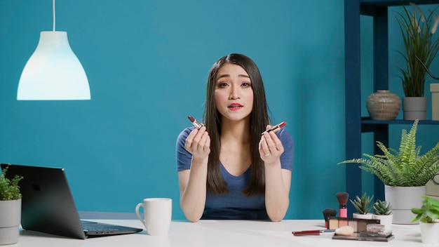 POV of asian influencer doing lipstick recommendation in studio, filming makeup review with cosmetics product on camera. Female blogger recording video for social media. Tripod shot.