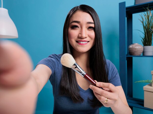 Pov of beauty influencer holding makeup brush showing to subscribers while recording cosmetics review for vlogging channel. Social media creator filming videoblog advertising make up product