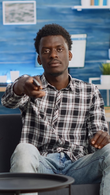 POV of black couple watching television on couch at home relaxing. African american woman eating popcorn and man switching channels with TV remote control while looking at camera