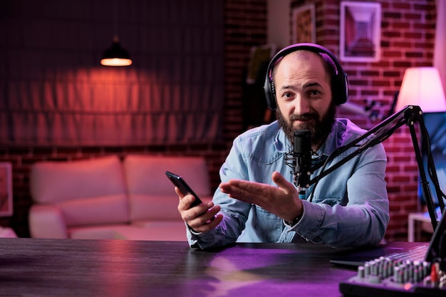 POV of content creator reviewing smartphone product on camera, filming podcast video in studio with neon lights. Online vlogger doing mobile phone recommendation on internet livestream.