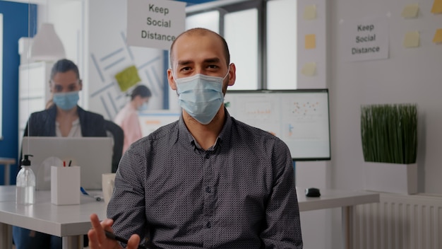 Pov entrepreneur man with protective face mask during zoom meeting call in new normal office. Freelancer talking into camera on remote online video conference call