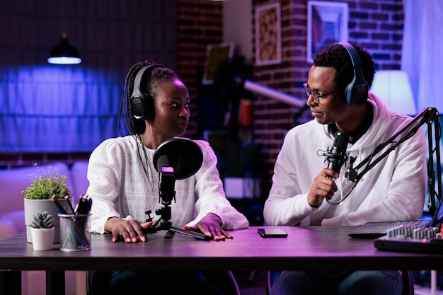 Free photo pov of man and woman recording live discussion on camera, doing podcast episode together. lifestyle influencer talking to female guest in studio with rpg neon lights and equipment.