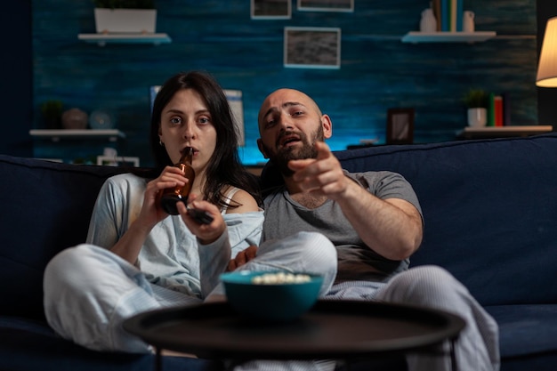 POV of man and woman switching television channels with TV remote control, doing movie selection to find fun film. Couple changing media program broadcast, doing leisure activity.