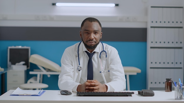 病院のオフィスでのオンラインビデオ通話会議の会議中に遠隔地の患者を聞いているアフリカ系アメリカ人のセラピスト医師のハメ撮り。投薬治療を説明する医師の男性。遠隔医療コールの概念
