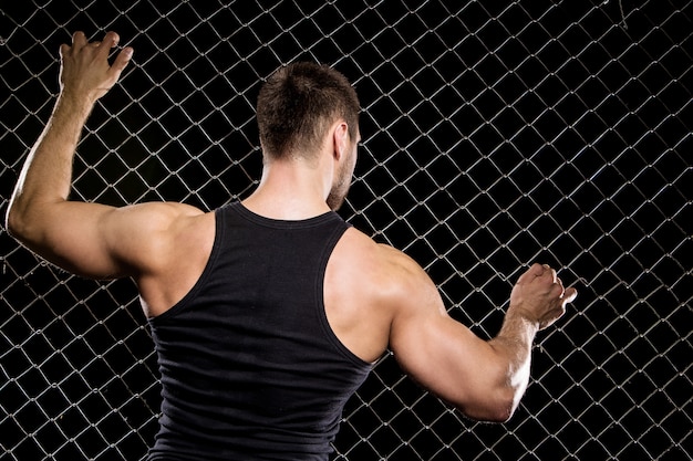 Powerful guy showing his muscles on fence  