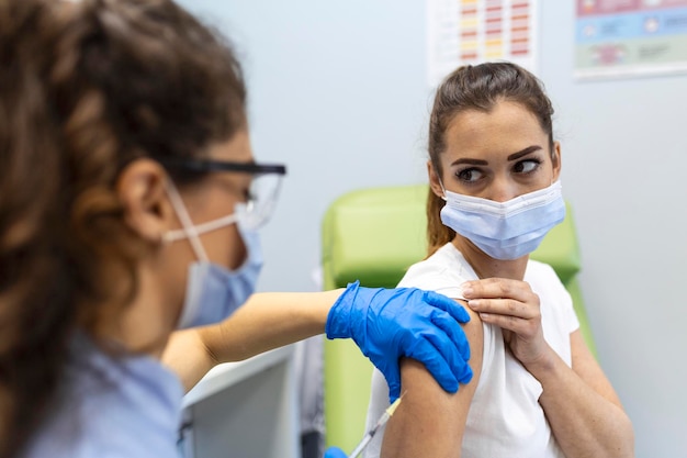 Practitioner vaccinating woman patient in clinic Doctor giving injection to woman at hospital Nurse holding syringe and inject Covid19 or coronavirus vaccineInjection covid vaccine concept