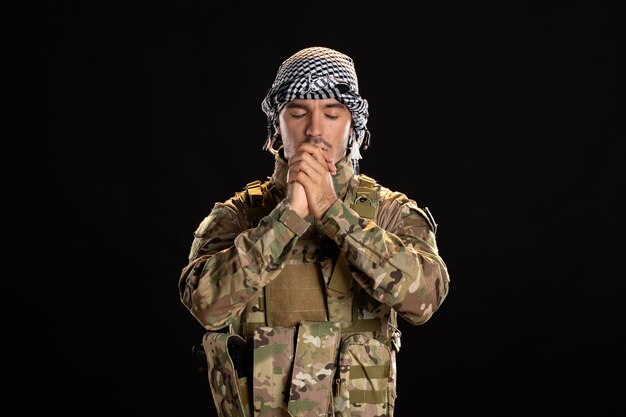 Praying male soldier in camouflage on a black wall