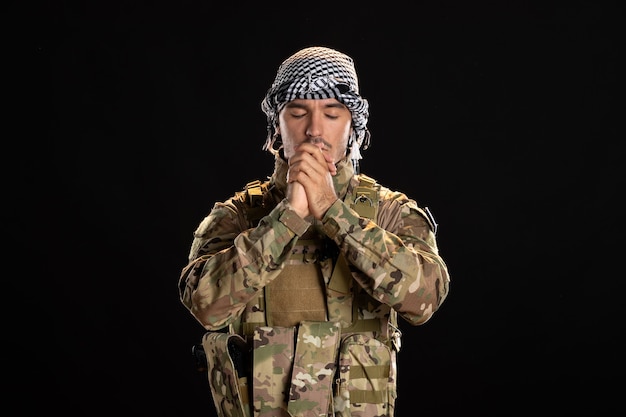 Бесплатное фото Молящийся мужчина-солдат в камуфляже на черной стене