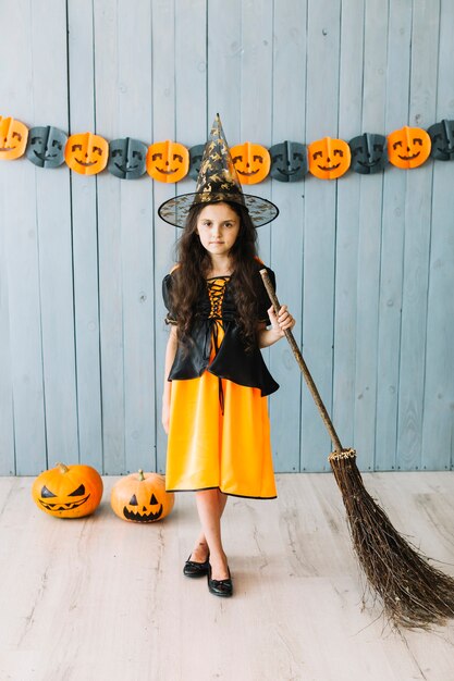 Pre-teen girl in pointy hat standing with broom