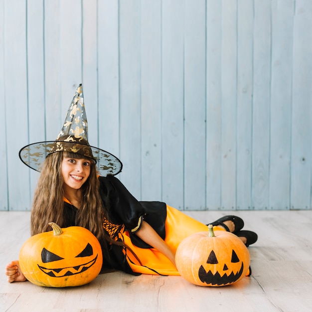 Pre-teen girl in witch costume lying on floor with pumpkins