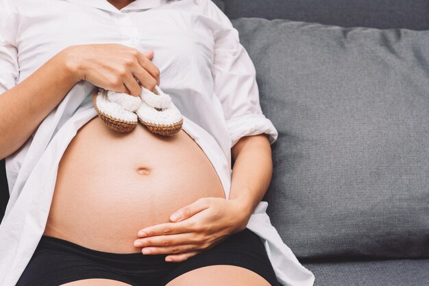 아기를 위한 아기 제품을 준비하는 뱃속에 신발 한 켤레를 들고 있는 임산부