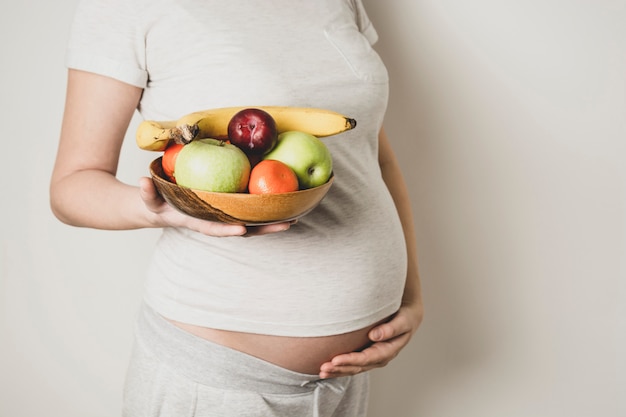 妊娠中​の​腹​、​健康​食品​の​女性​、​手​で​果物​の​ボウル​。​コピー​スペース​。