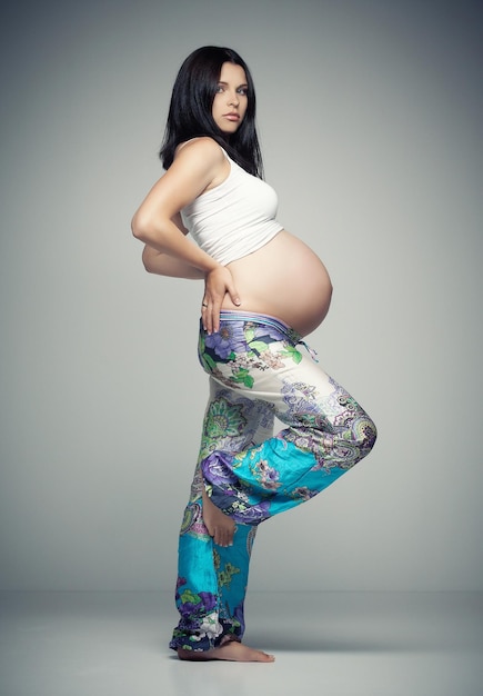 Pregnant brunette woman in sportswear posing in studio.