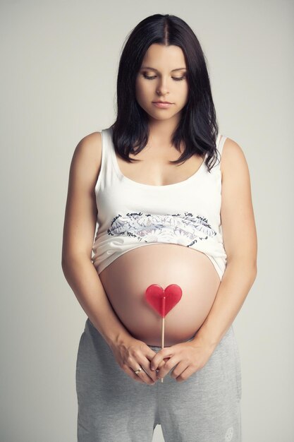 Pregnant brunette woman with red heart candy.