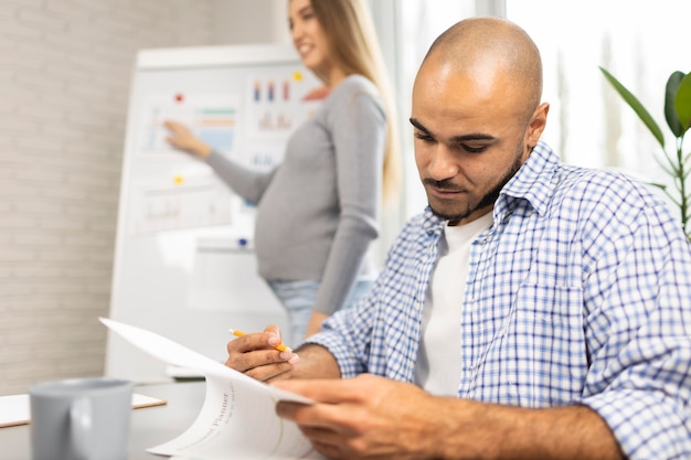 Pregnant businesswoman giving presentation in the office while coworker takes notes