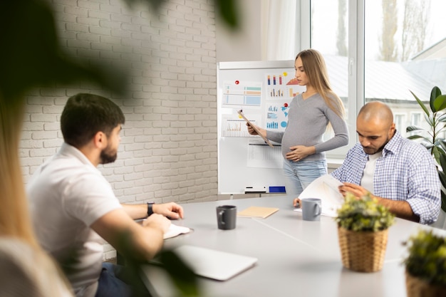 Pregnant businesswoman giving presentation while coworkers take notes