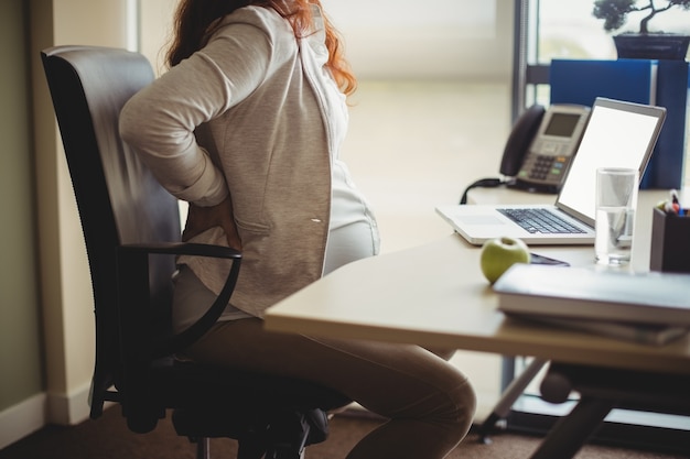 Pregnant businesswoman holding her back while sitting on chair