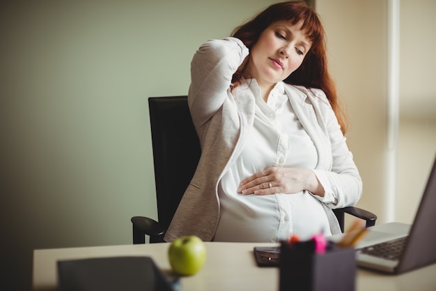 Free photo pregnant businesswoman holding her back while sitting on chair