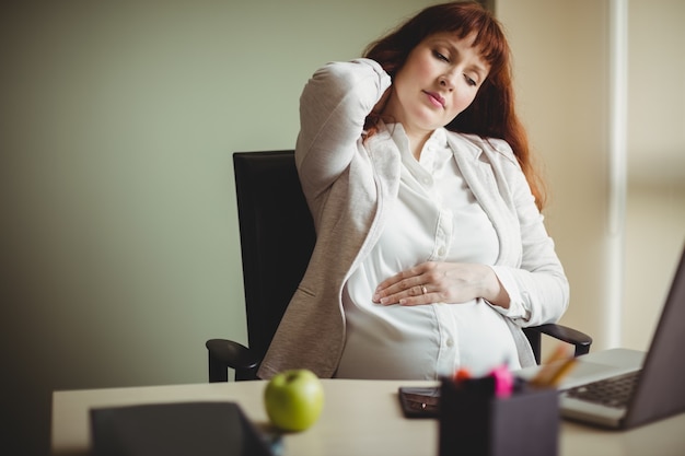 Pregnant businesswoman holding her back while sitting on chair