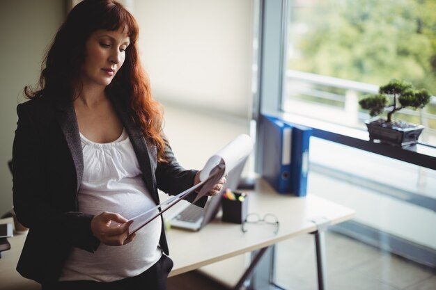 Foto gratuita donna di affari incinta che legge documenti cartacei