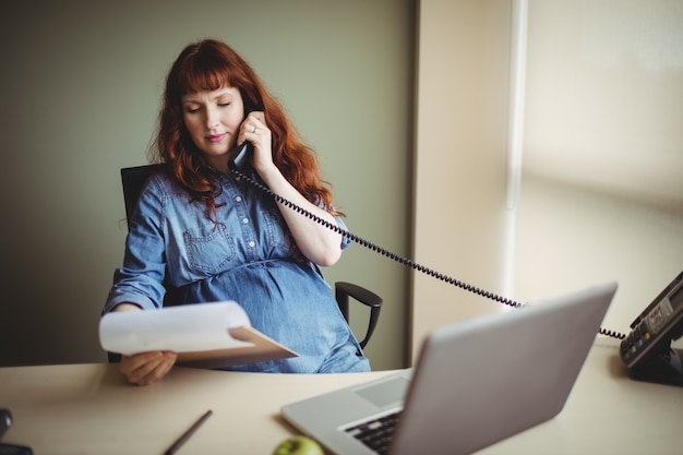 Pregnant businesswoman talking on telephone while working